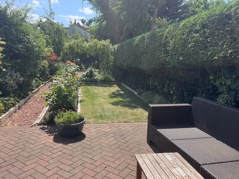 A kept garden: a clipped hedge, lawn, rose bed and herringbone brick patio